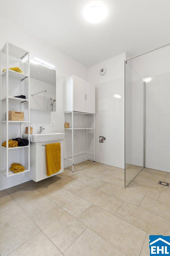 Helles Badezimmer mit großer ebenerdiger Dusche, modernem Waschbecken und Fliesenboden.