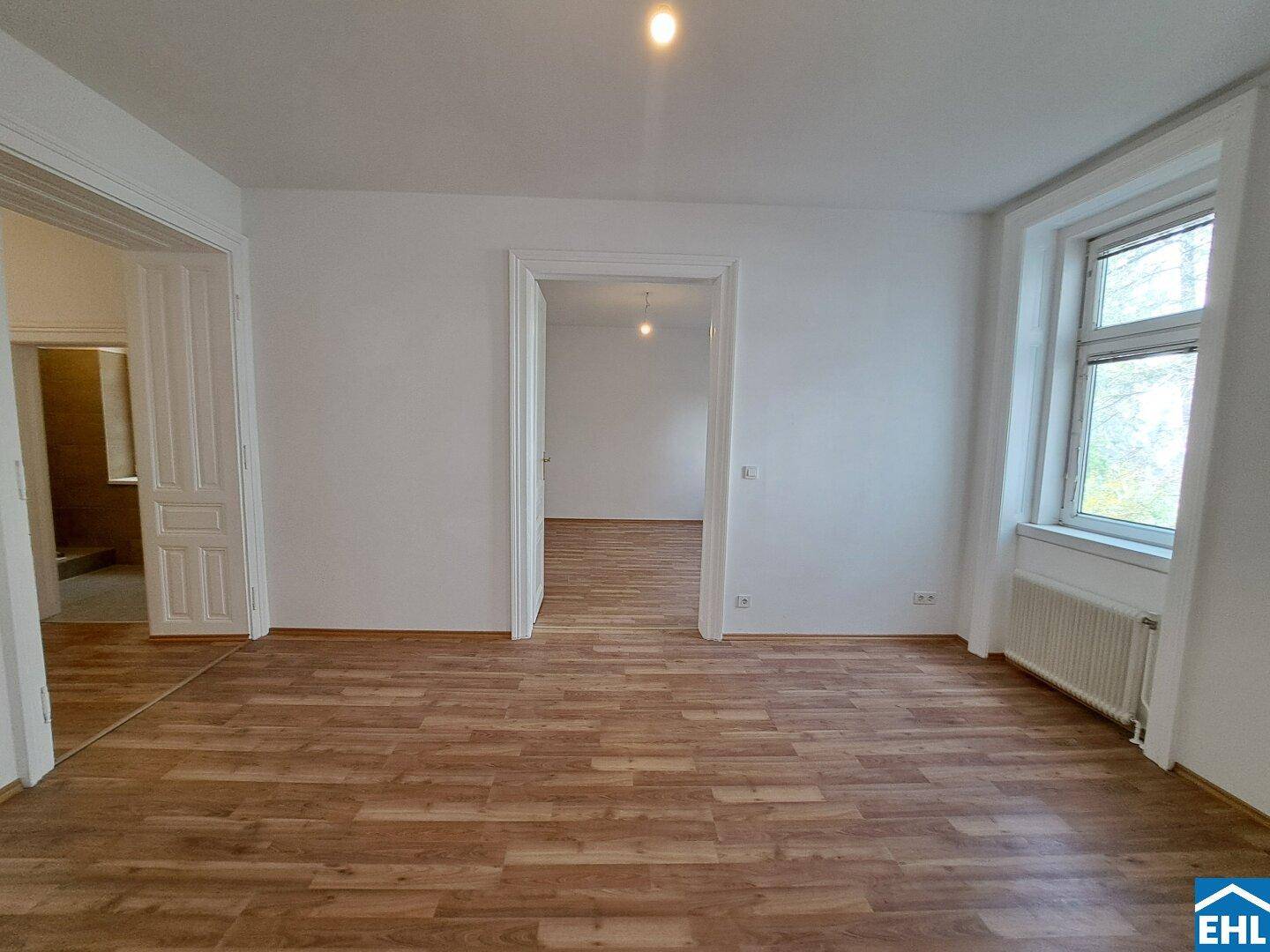 Lichtdurchflutetes Zimmer mit Laminatboden und einem großen Fenster, das viel Tageslicht hereinlässt.