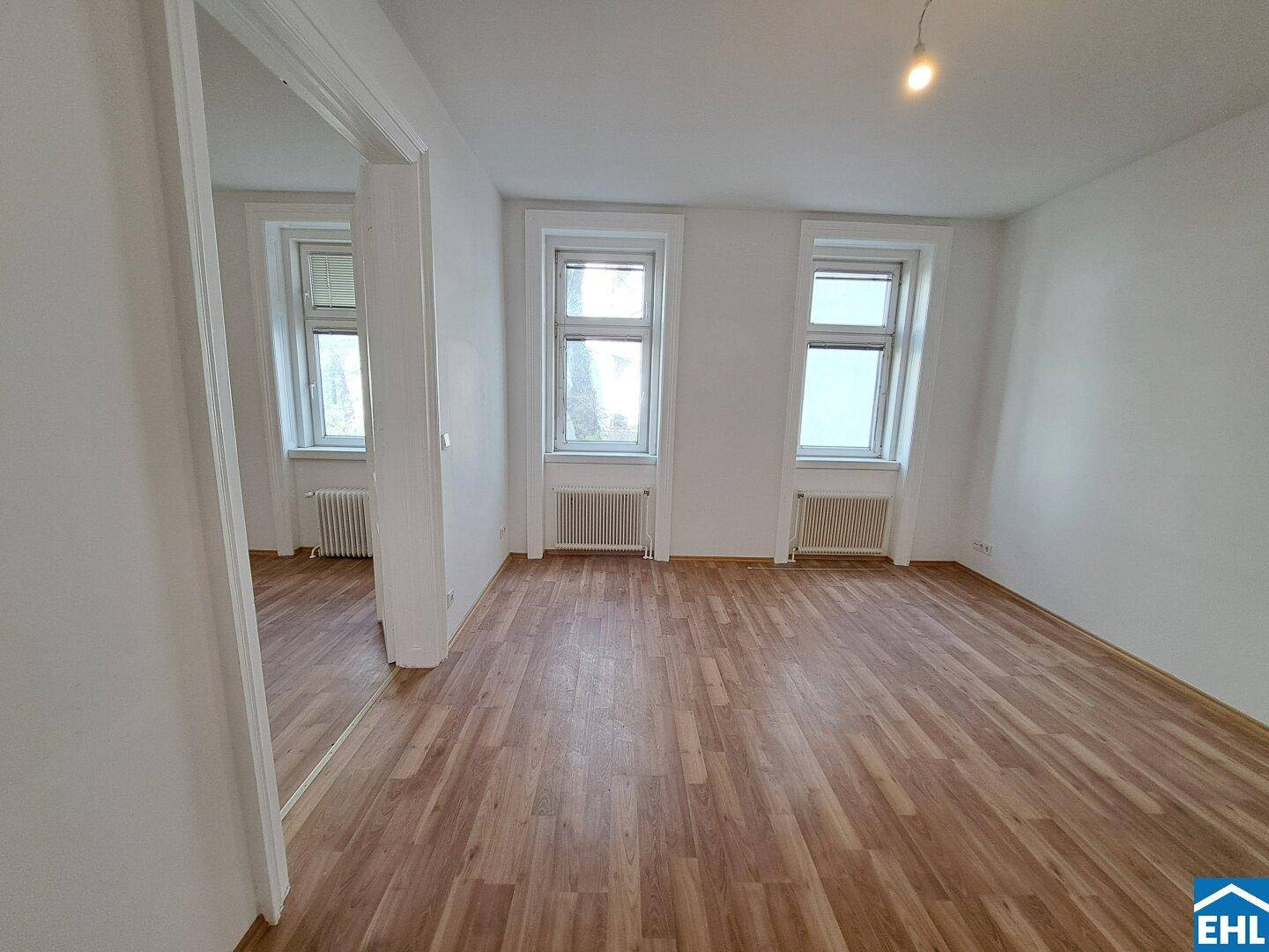 Geräumiges, helles Zimmer mit Laminatboden, zwei Fenstern und Heizkörpern, ideal als Wohn- oder Schlafzimmer.