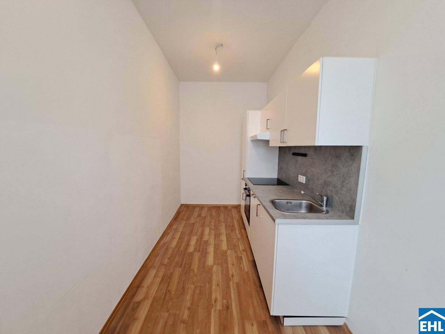 Kompakte Einbauküche mit weißen Fronten, Spüle und modernen Geräten, ideal für kleine Wohnungen.