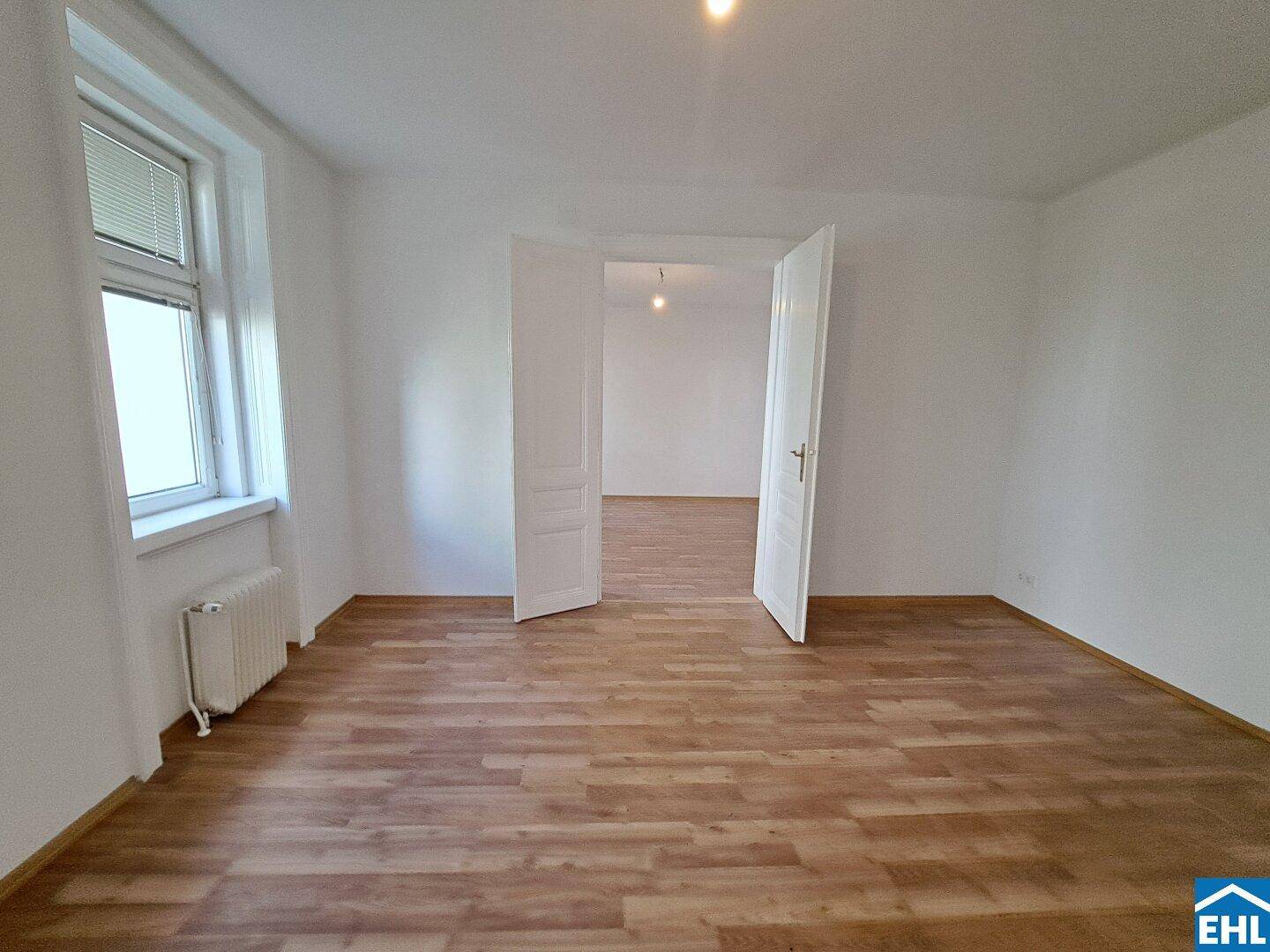 Helles Zimmer mit Laminatboden und großen Fenstern, die viel Tageslicht in den Raum lassen.