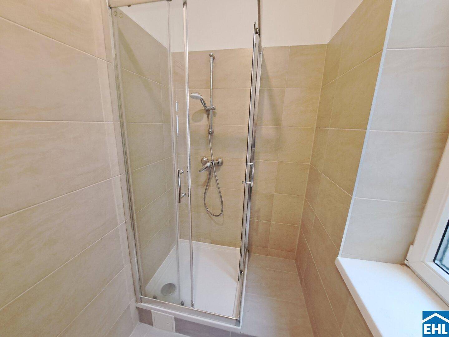 Modernes Badezimmer mit beigefarbenen Fliesen und einer Duschkabine mit Glaswänden.