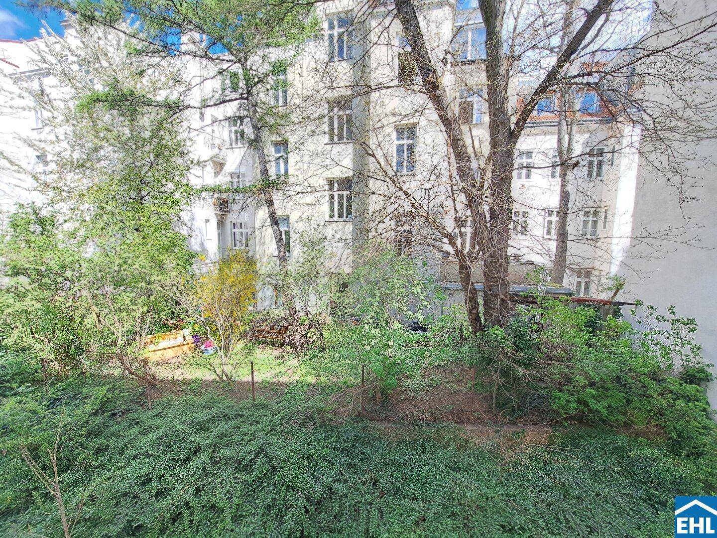 Blick auf einen grünen Innenhof mit Bäumen und Sträuchern, umgeben von Wohngebäuden.