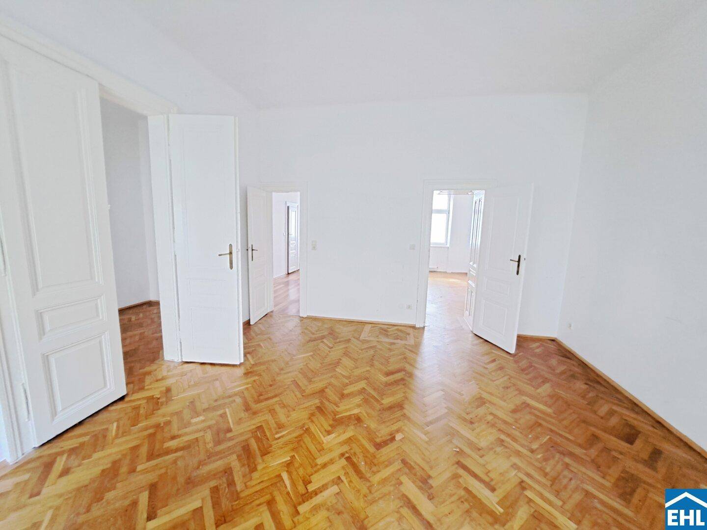 Geräumiges Zimmer mit Fischgrätparkett und mehreren Türen, bereit zur individuellen Gestaltung.