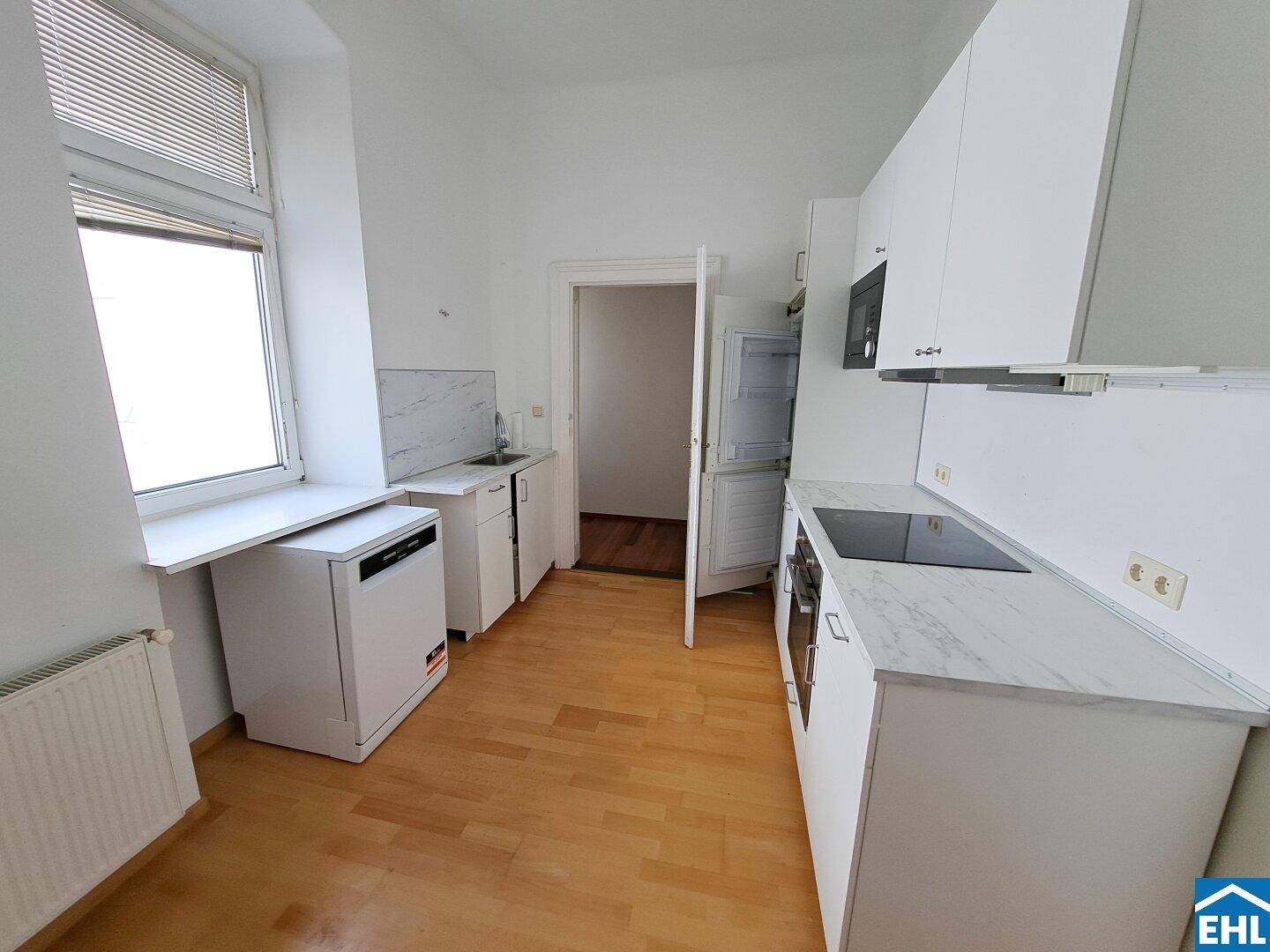 Funktionale Küche mit weißen Schränken, integrierten Geräten und einem Fenster.