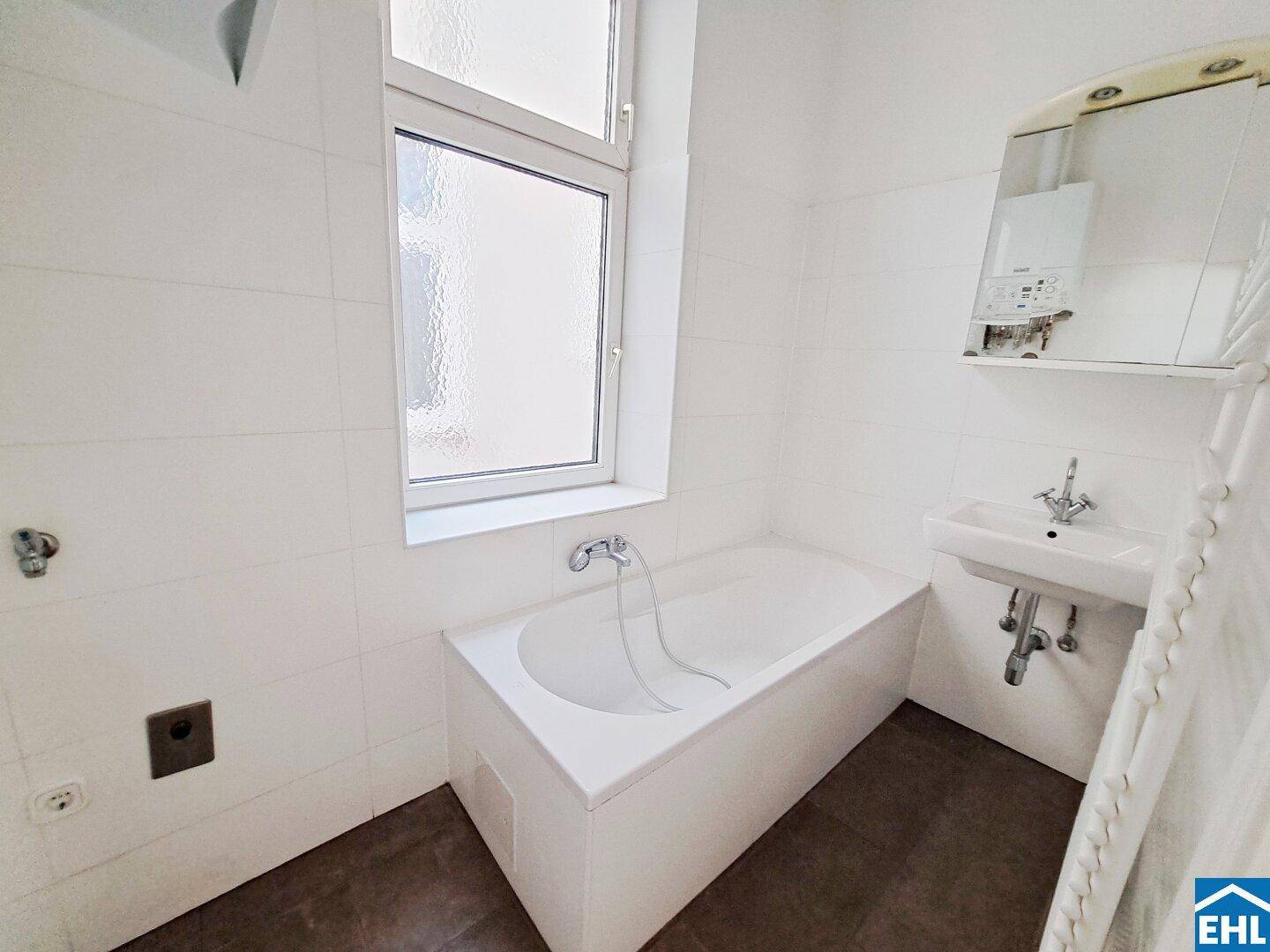 Helles Badezimmer mit Badewanne, Waschbecken und einem Fenster für natürliche Belüftung.