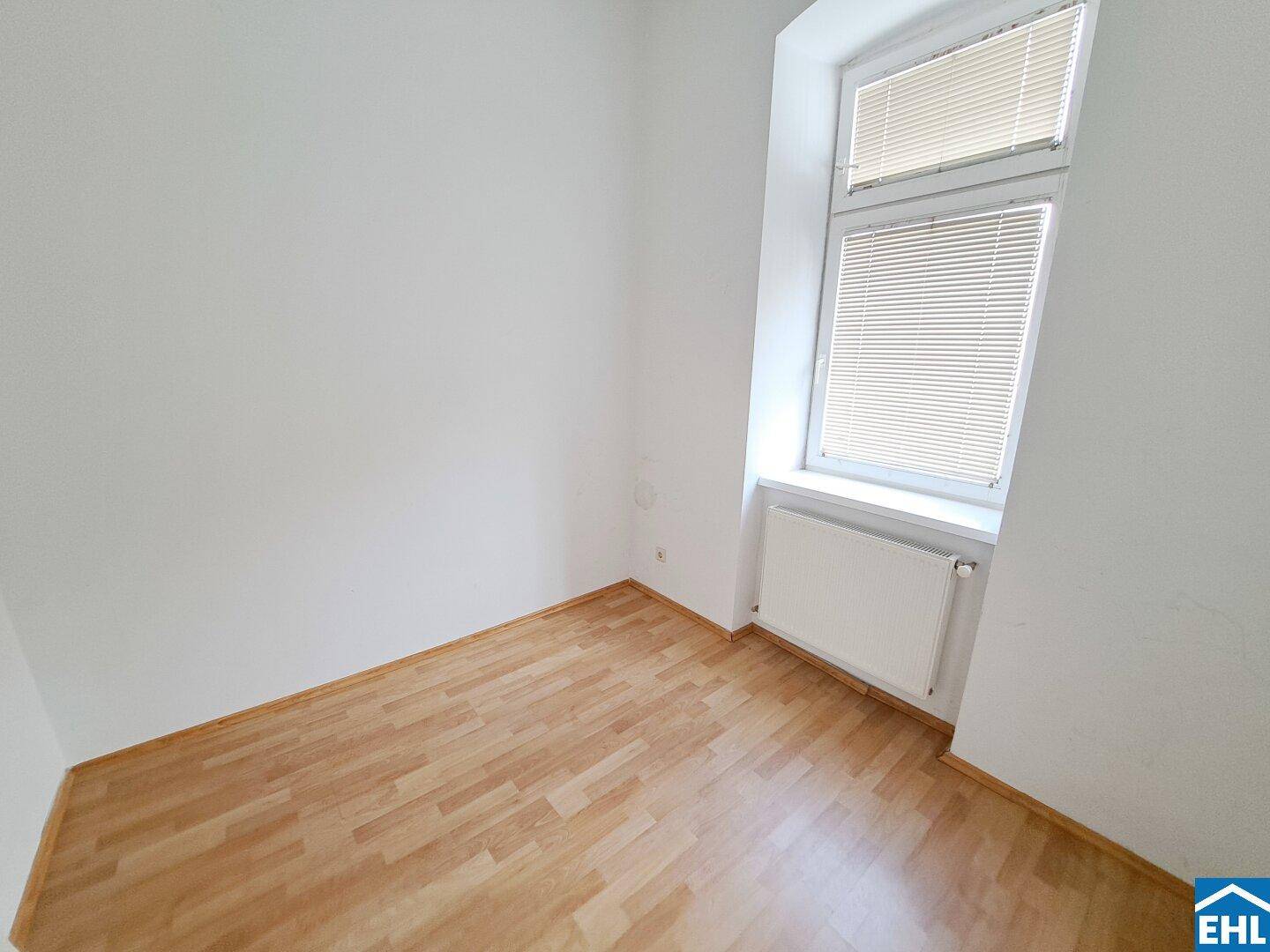 Kleineres Zimmer mit Laminatboden und einem Fenster mit Jalousien, ideal als Schlaf- oder Arbeitszimmer.