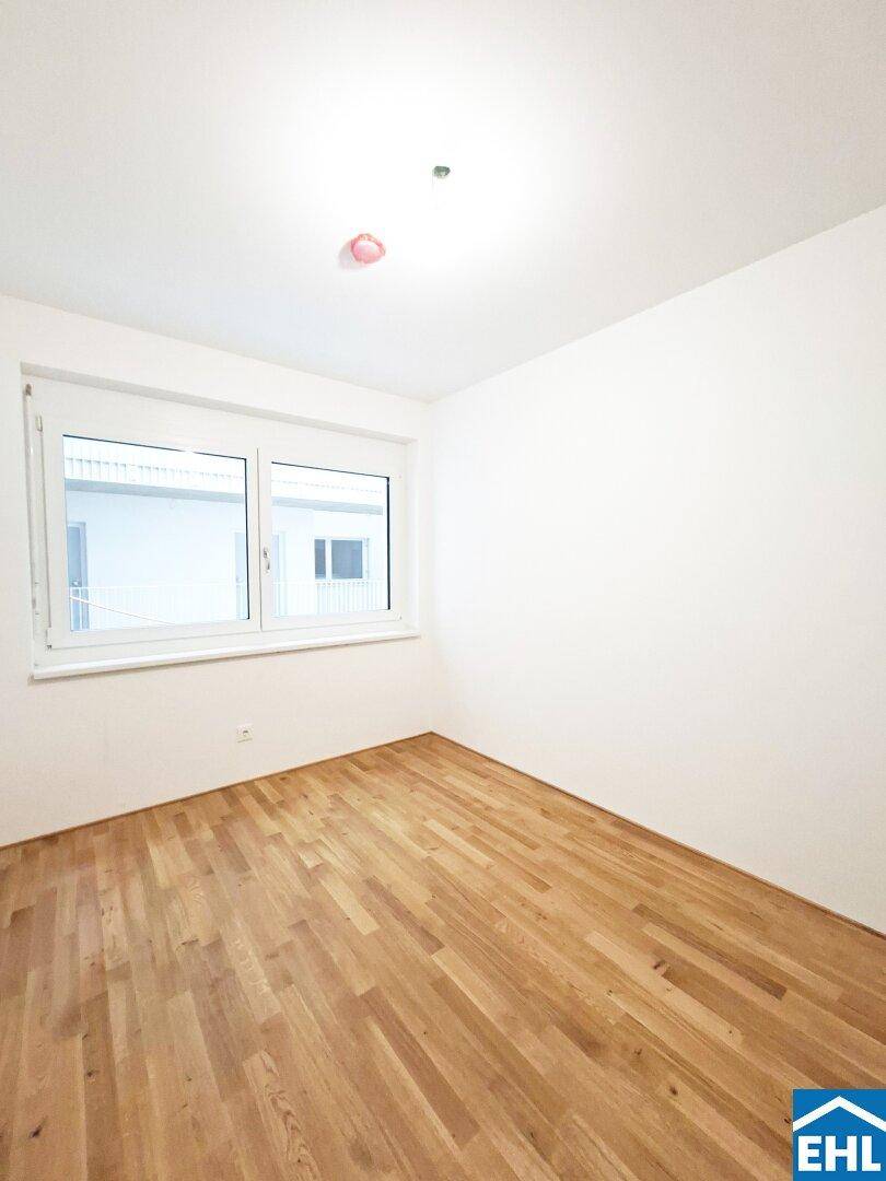 Lichtdurchflutetes Zimmer mit großen Fenstern und hellem Parkettboden, bereit für individuelle Gestaltung.
