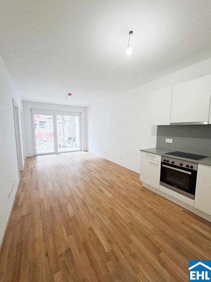 Heller Wohnbereich mit offener Küche und Zugang zu einem Balkon, ausgestattet mit Parkettboden.