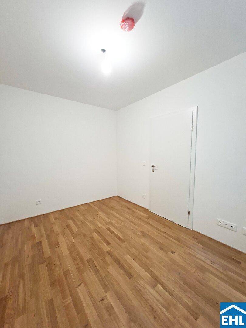 Leeres Zimmer mit hellem Parkettboden und weißer Tür, bereit zum Einrichten.