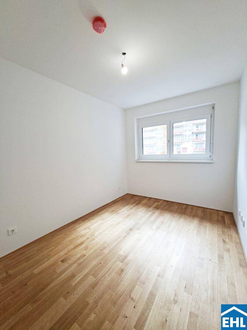 Leeres Zimmer mit Parkettboden und großem Fenster, bietet viel Tageslicht und eine angenehme Atmosphäre.