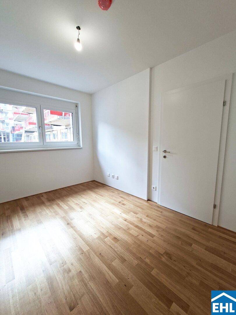 Geräumiges Zimmer mit Parkettboden, weiß gestrichenen Wänden und viel Tageslicht.