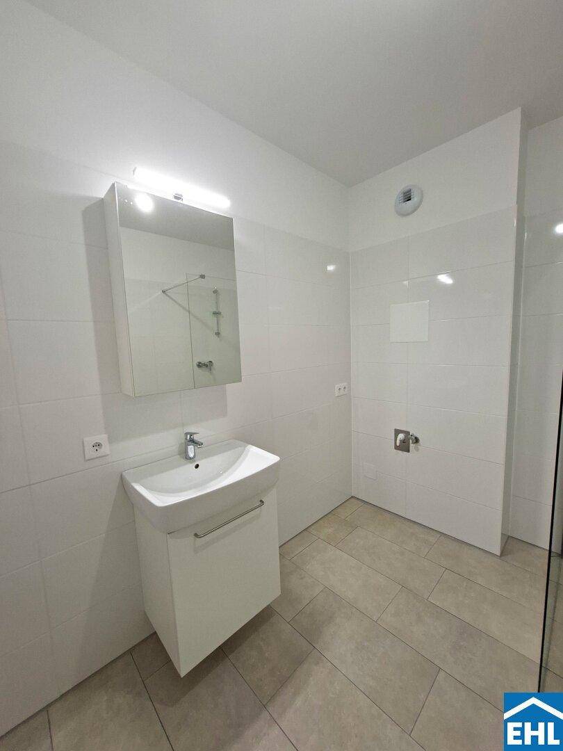 Modernes Badezimmer mit weißem Waschtisch, Spiegelschrank und gefliesten Wänden.