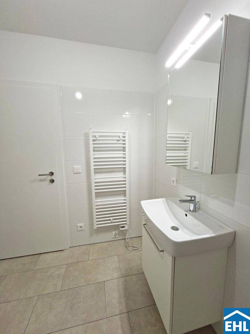 Helles Badezimmer mit Waschtisch, Spiegelschrank und beheiztem Handtuchhalter, modern ausgestattet.