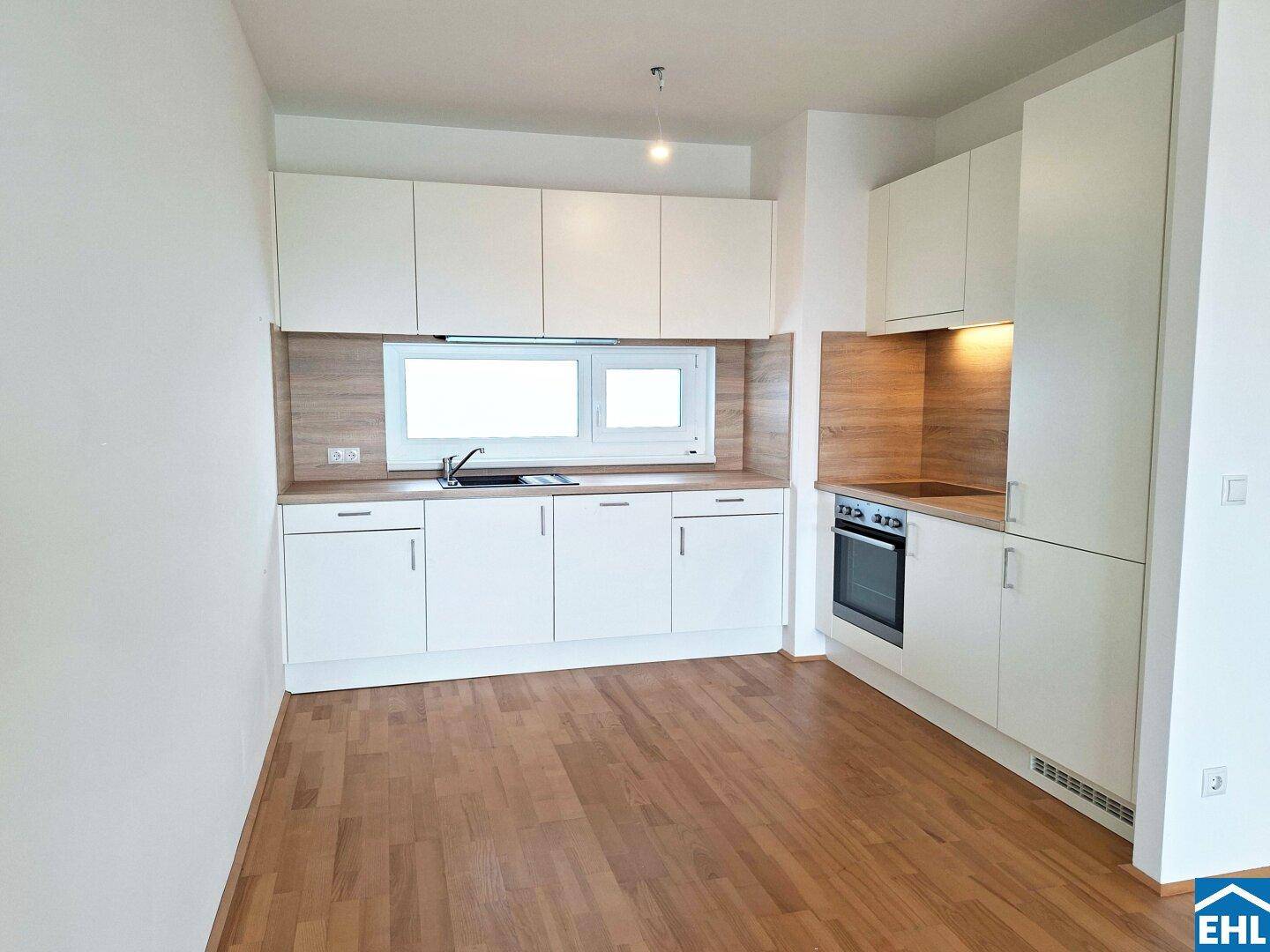 Moderne Einbauküche mit weißen Schränken, Holzoptik-Arbeitsplatte und Fenster für Tageslicht.