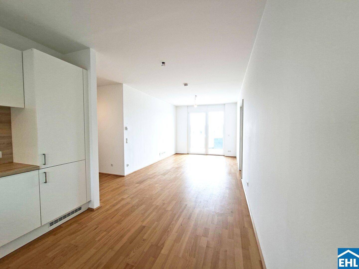 Lichtdurchfluteter offener Wohnbereich mit Parkettboden und Zugang zu einem Außenbereich.
