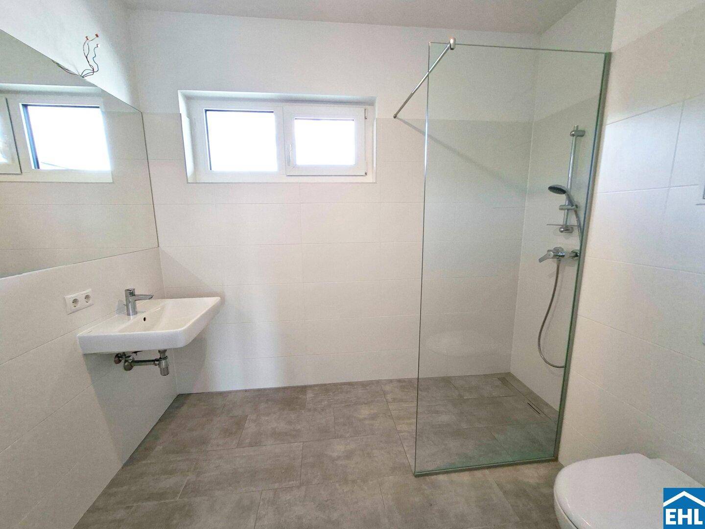 Modernes Badezimmer mit ebenerdiger Dusche, Waschbecken und Fenster für Tageslicht.