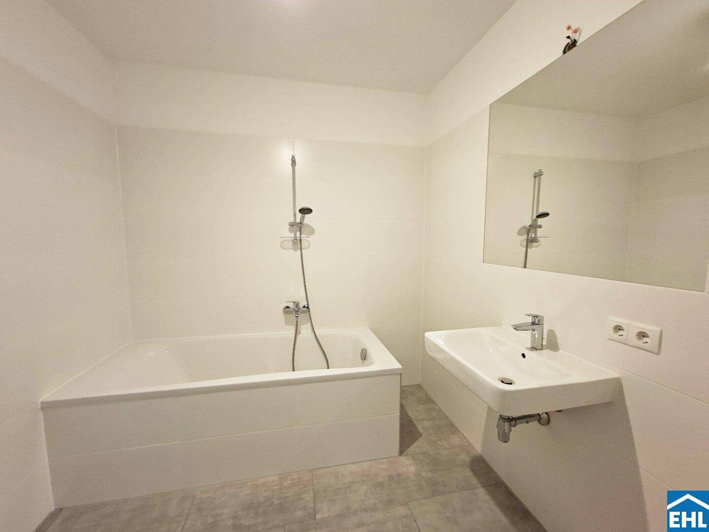 Helles Badezimmer mit Badewanne, Waschbecken und großem Spiegel, in neutralen Farben gehalten.