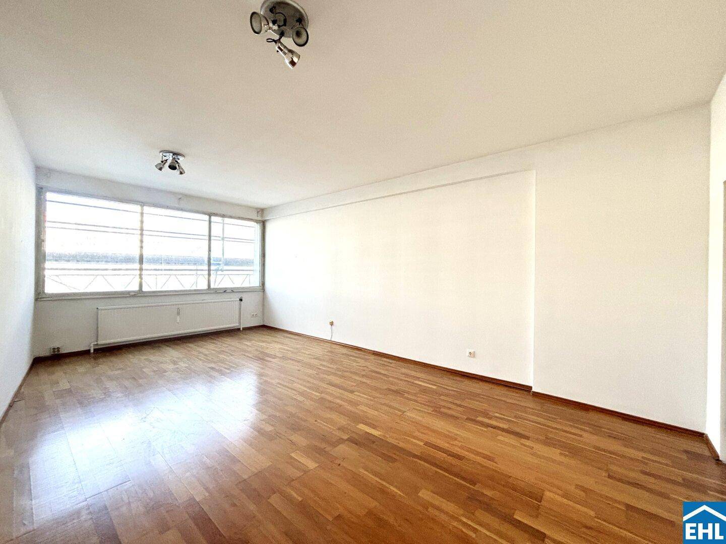 Geräumiges, helles Zimmer mit Holzparkett und breiter Fensterfront, ideal für Wohnzwecke.