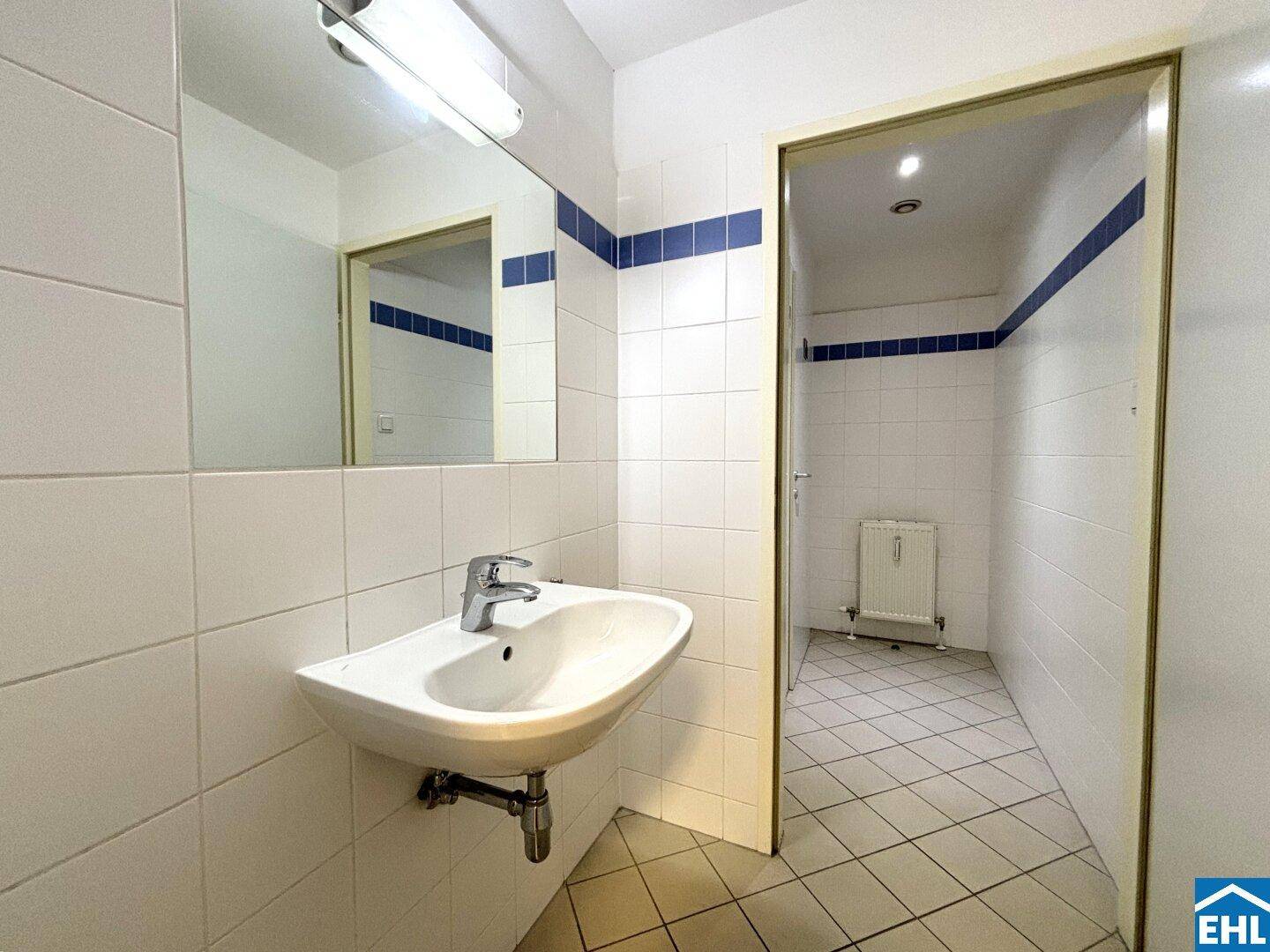 Kleiner Waschraum mit Fliesenboden, Einzelwaschbecken und Spiegel.