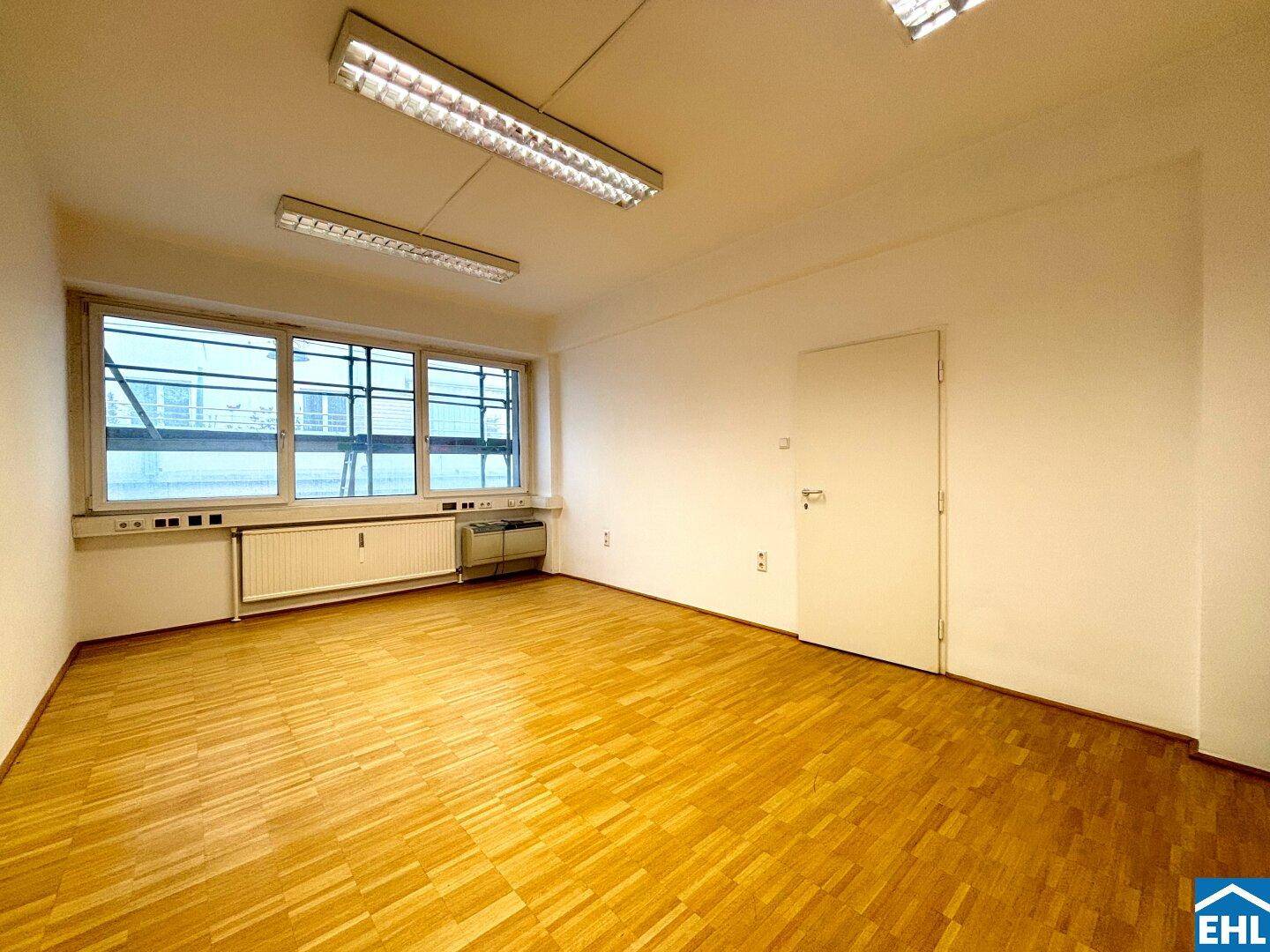 Geräumiger, leerer Raum mit Parkettboden, Fenstern und einer Tür.