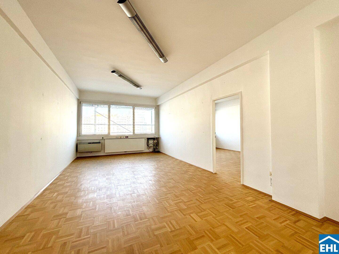 Geräumiges, helles Zimmer mit Parkettboden und Zugang zu einem weiteren Raum.