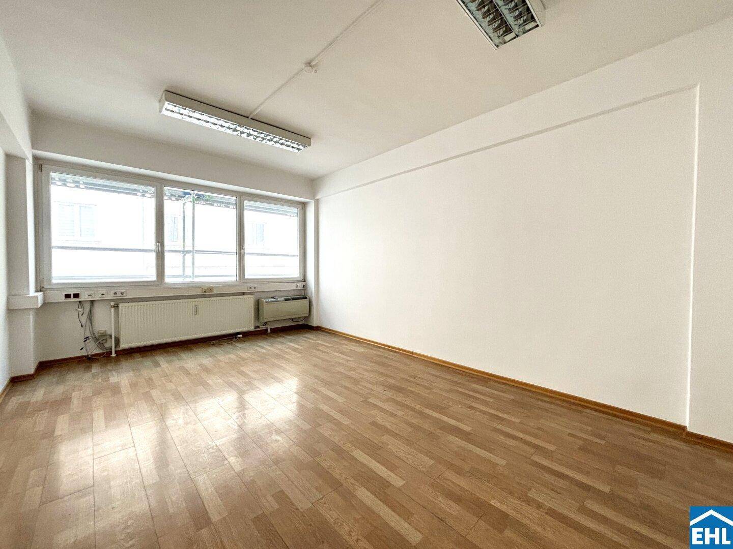 Geräumiger, heller Raum mit Parkettboden und breiter Fensterfront, bietet viel Tageslicht.