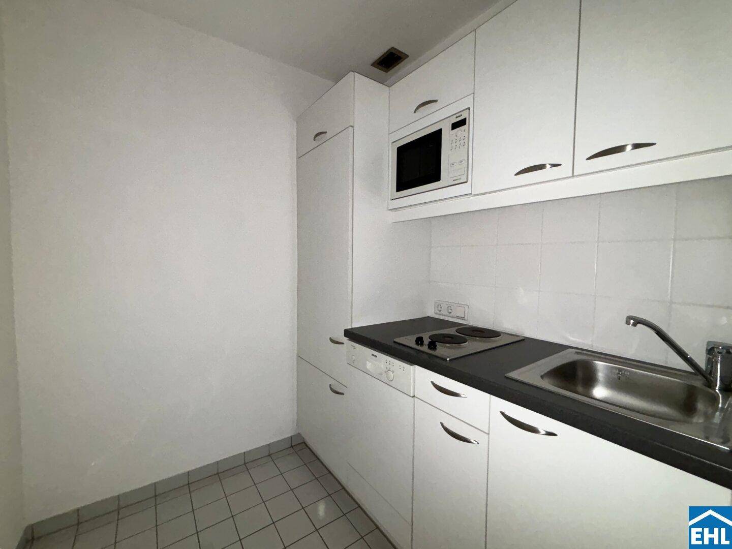 Kleine Einbauküche mit weißen Schränken, Spüle und Kochfeld, praktisch und funktional.