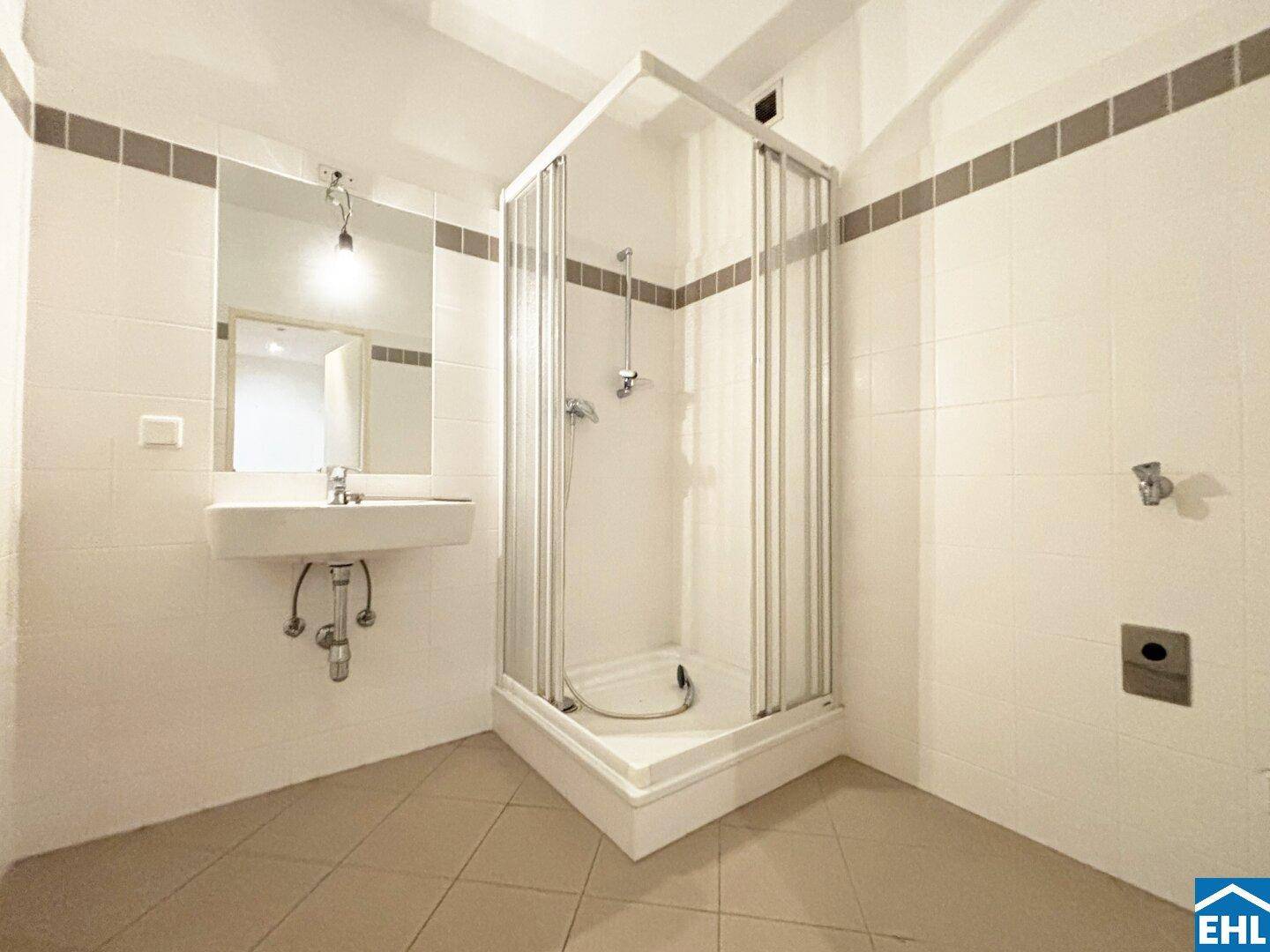 Badezimmer mit Duschkabine, Waschbecken und weißen Fliesen, in gutem Zustand.