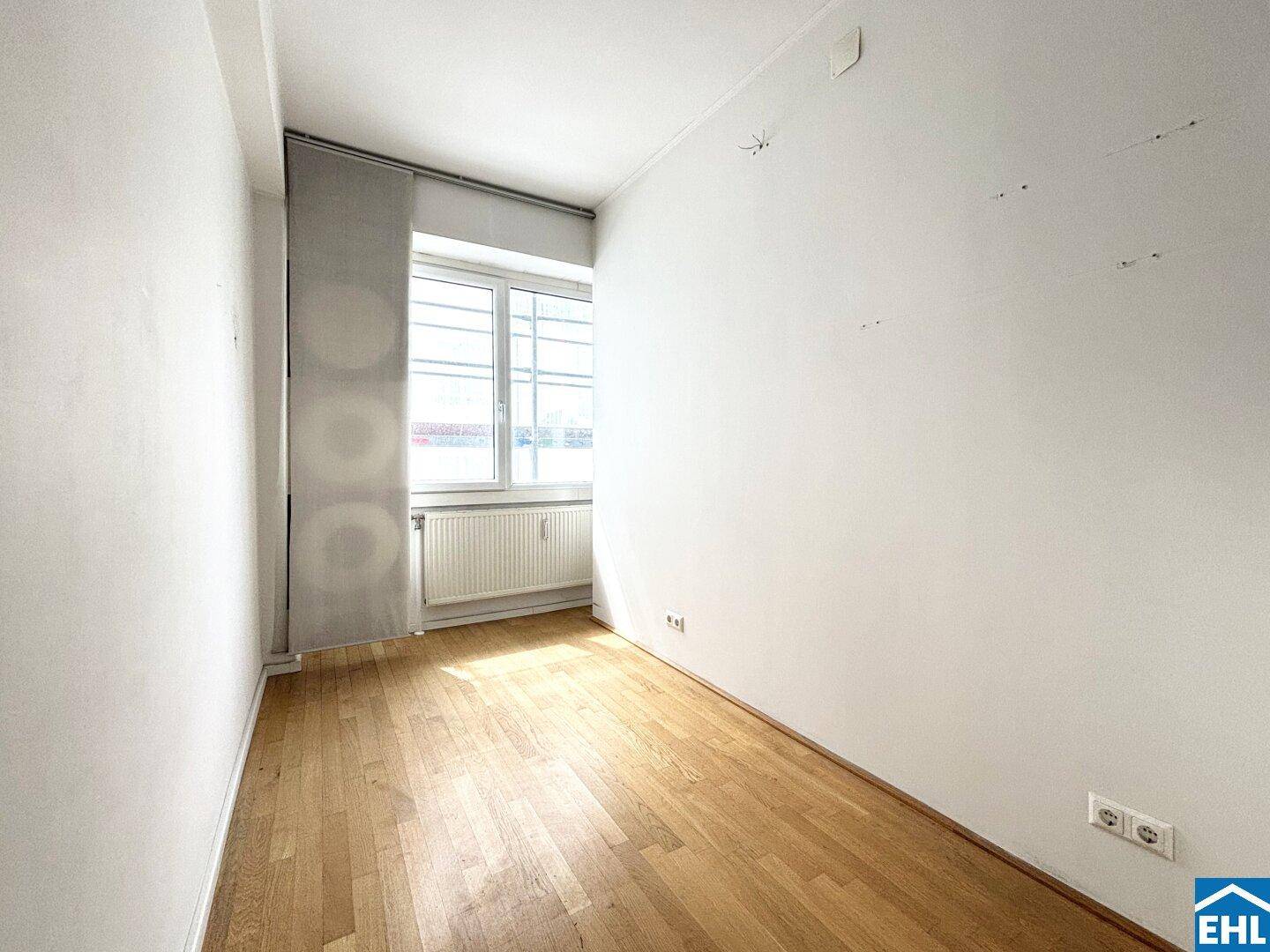 Lichtdurchflutetes Zimmer mit Holzparkettboden und großem Fenster, bereit zur individuellen Gestaltung.