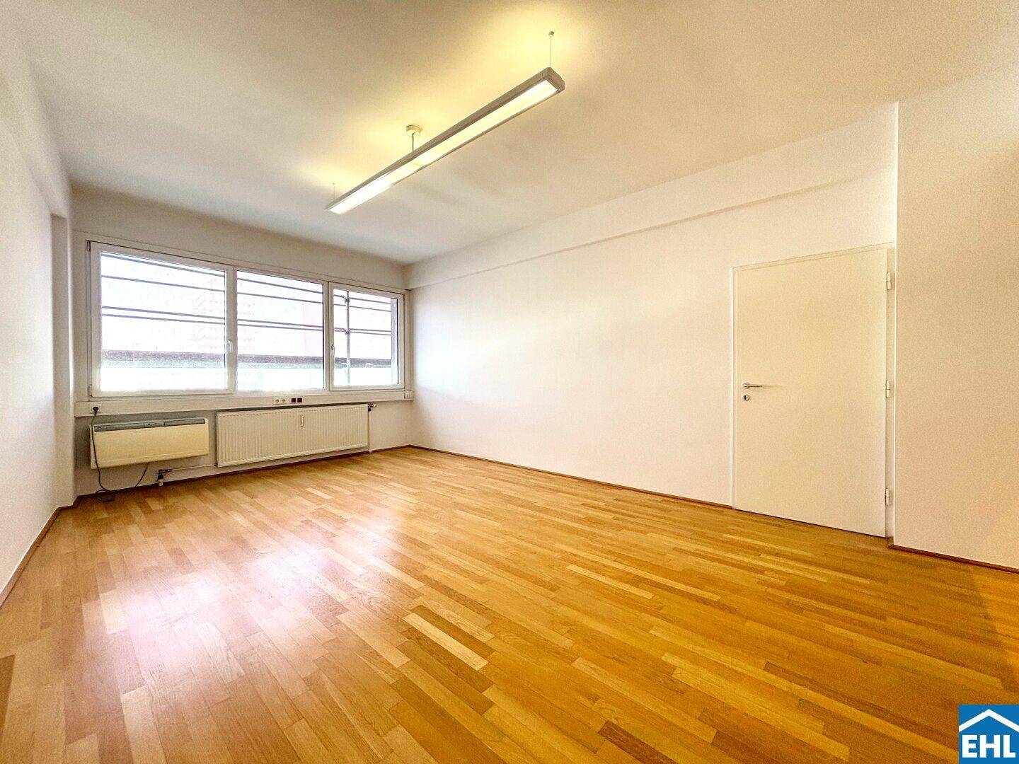 Heller Raum mit Holzparkettboden und großen Fenstern, ideal als Wohn- oder Arbeitsbereich.