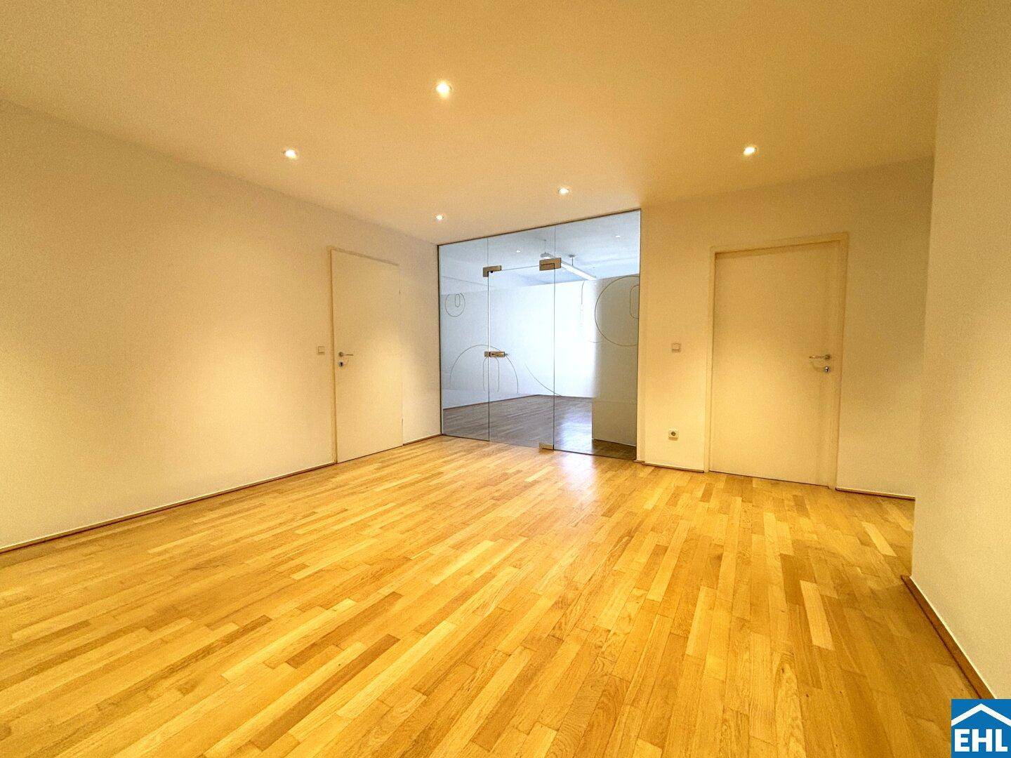 Heller Raum mit Holzparkett und Glastür, ausgestattet mit modernen Deckenspots.