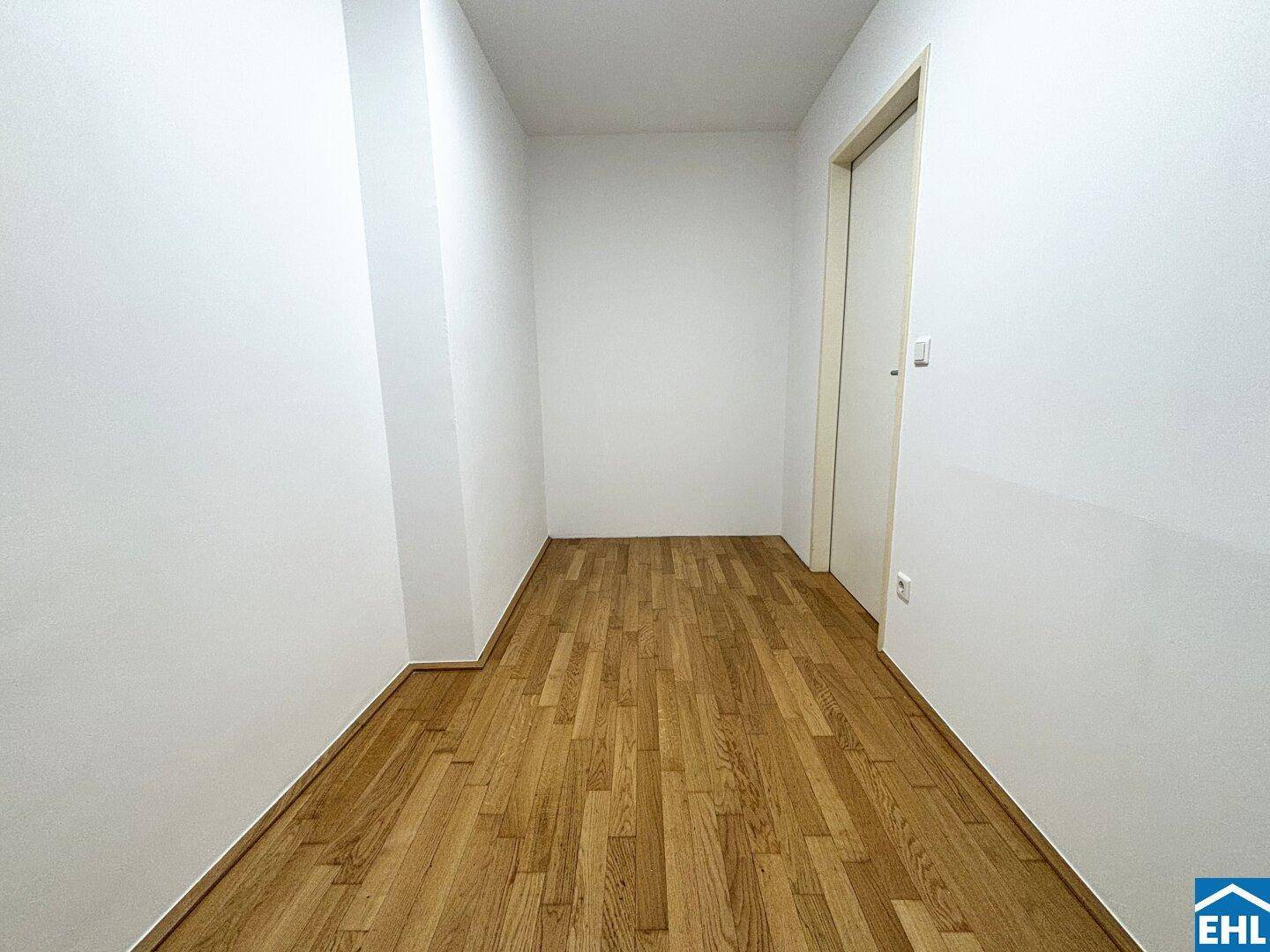 Schmaler Flur mit Holzparkettboden und weißen Wänden, der zu weiteren Räumen führt.