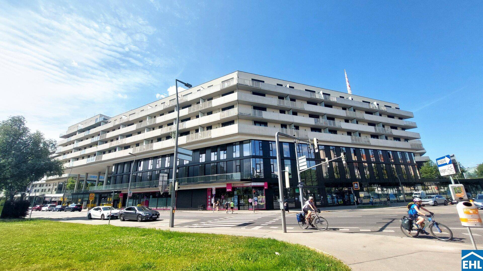 Modernes Mehrzweckgebäude mit Wohnungen, Balkonen und Geschäftsflächen im Erdgeschoss an einer belebten Straße.