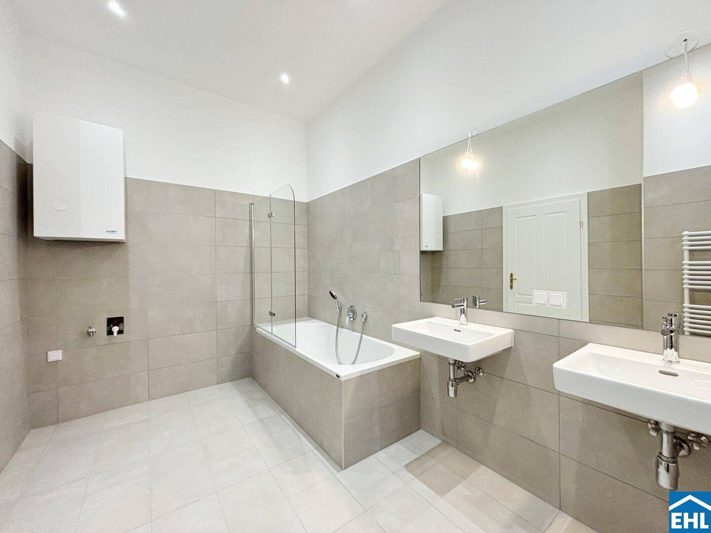 Modernes Badezimmer mit Doppelwaschbecken, Badewanne und großen Fliesen.