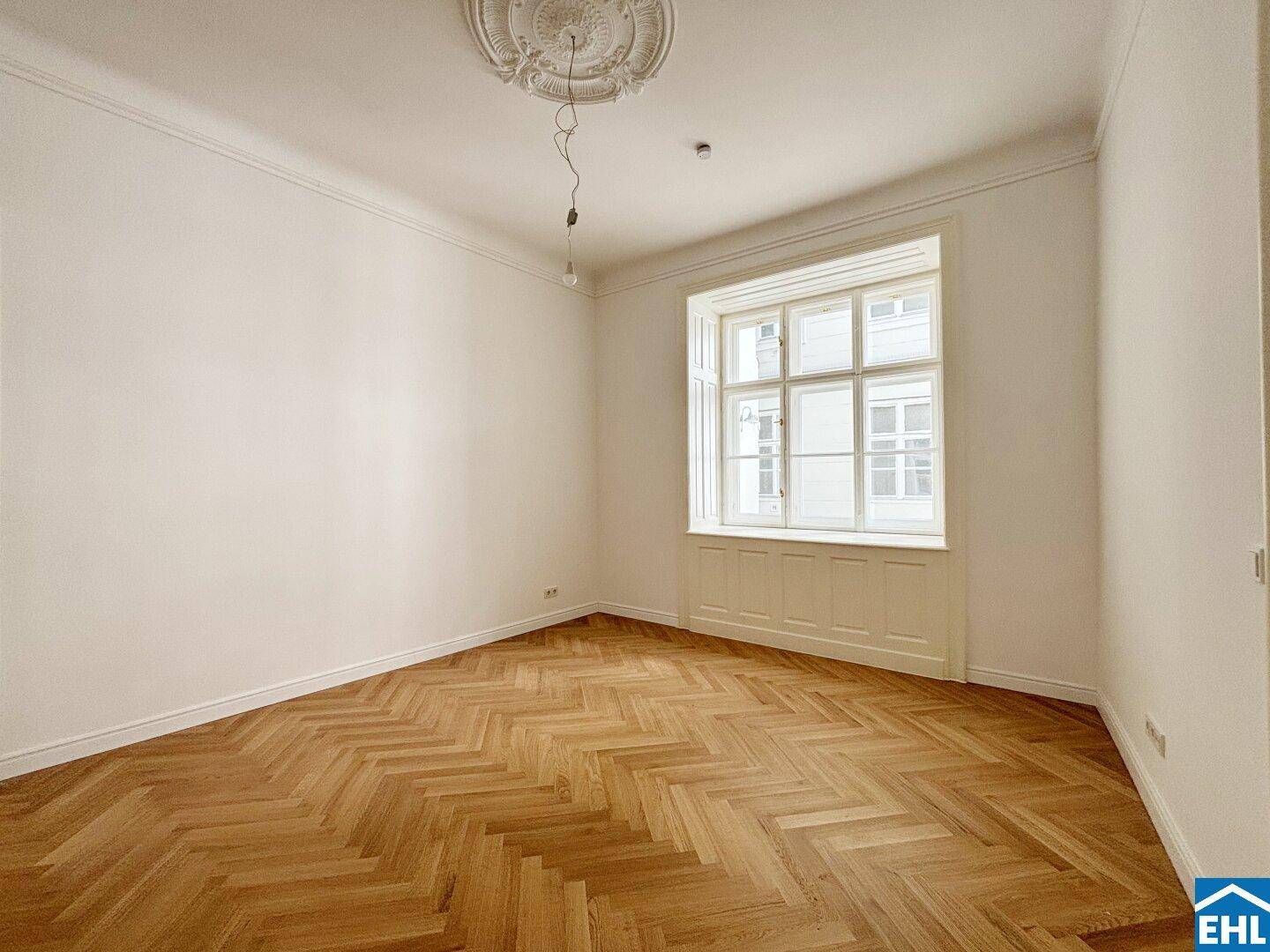 Geräumiges Zimmer mit klassischem Fischgrätparkett und einem großen Fenster.