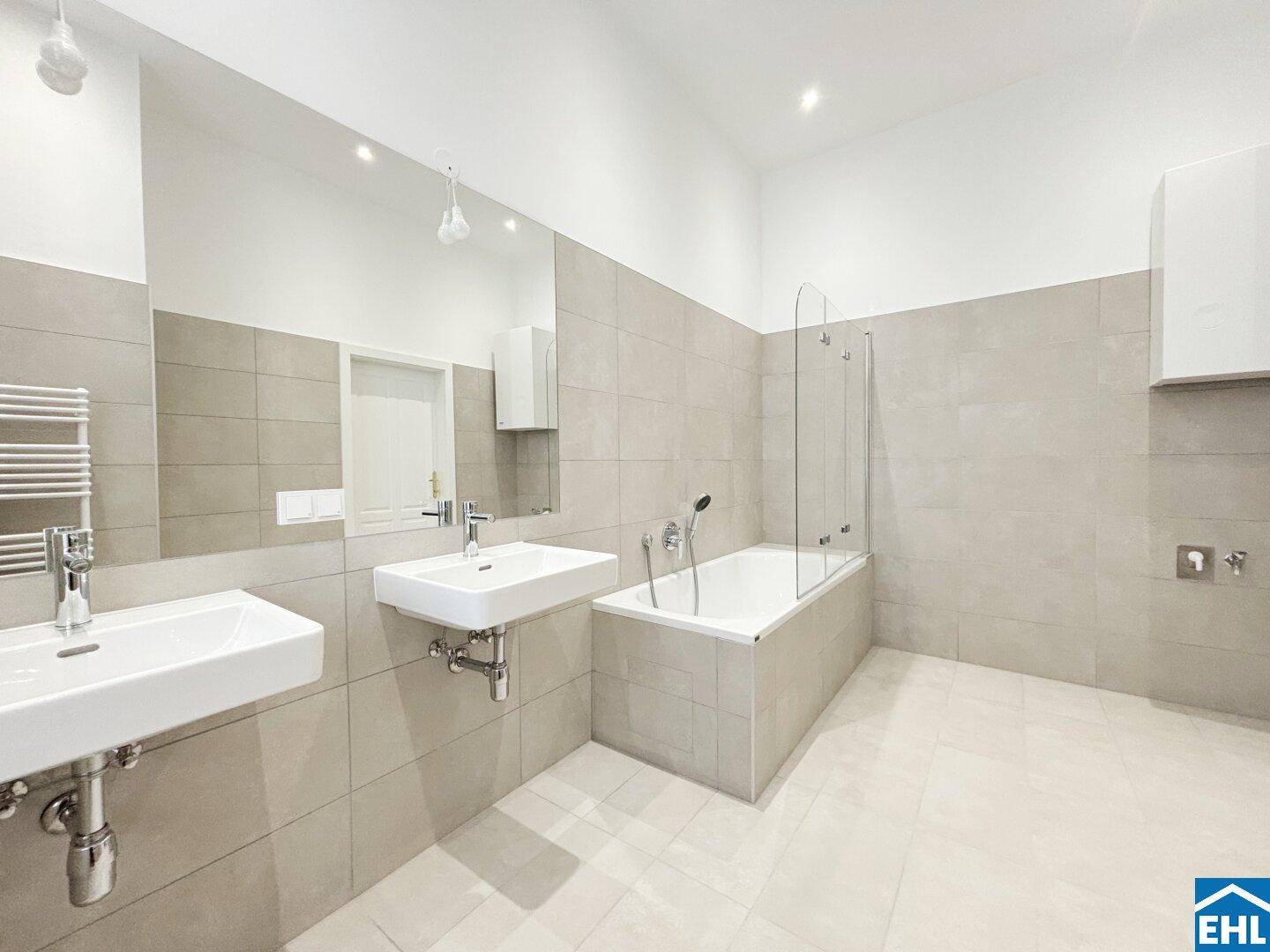 Modernes Badezimmer mit Doppelwaschbecken, Badewanne und Dusche, ausgestattet mit großen Fliesen und Spiegel.