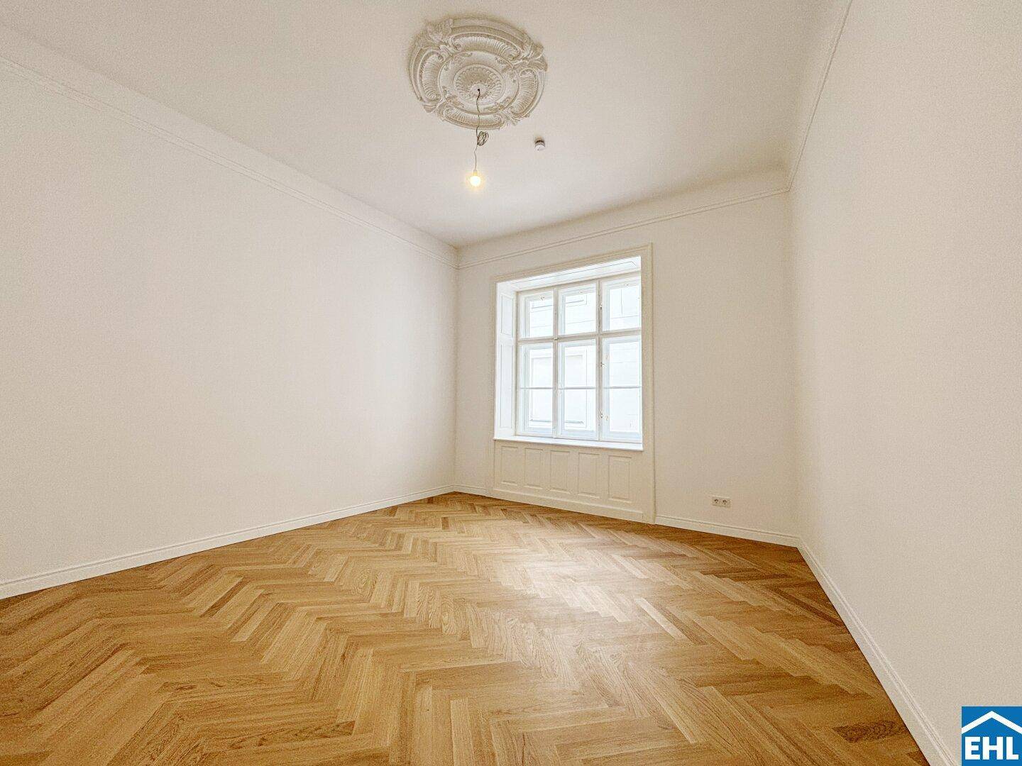 Lichtdurchflutetes Zimmer mit elegantem Fischgrätparkett und Stuckdecke, ideal für vielfältige Nutzungsmöglichkeiten.