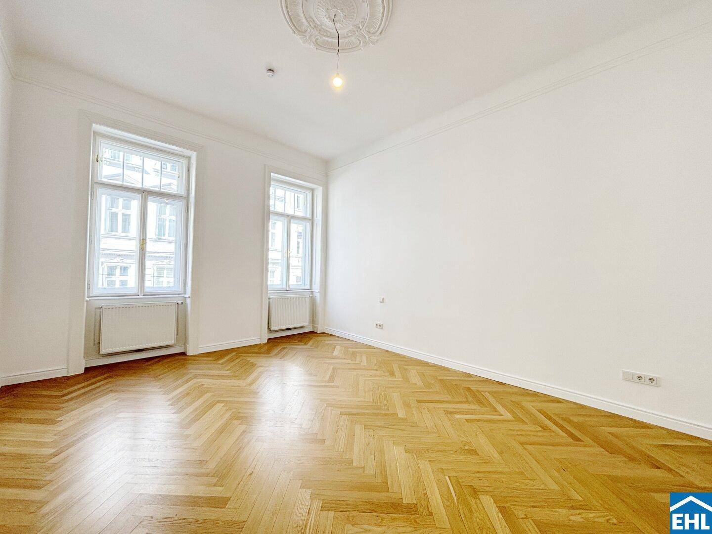 Geräumiges Zimmer mit elegantem Fischgrätparkett und dekorativer Stuckdecke.
