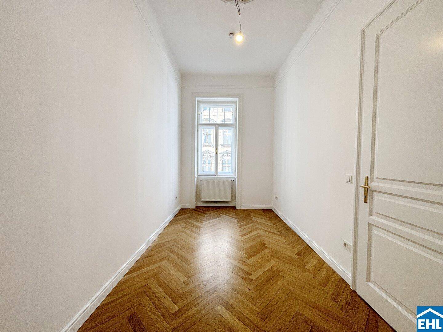 Schmaler Raum mit Fischgrätparkett und einem Fenster, geeignet als Schlaf- oder Arbeitszimmer.