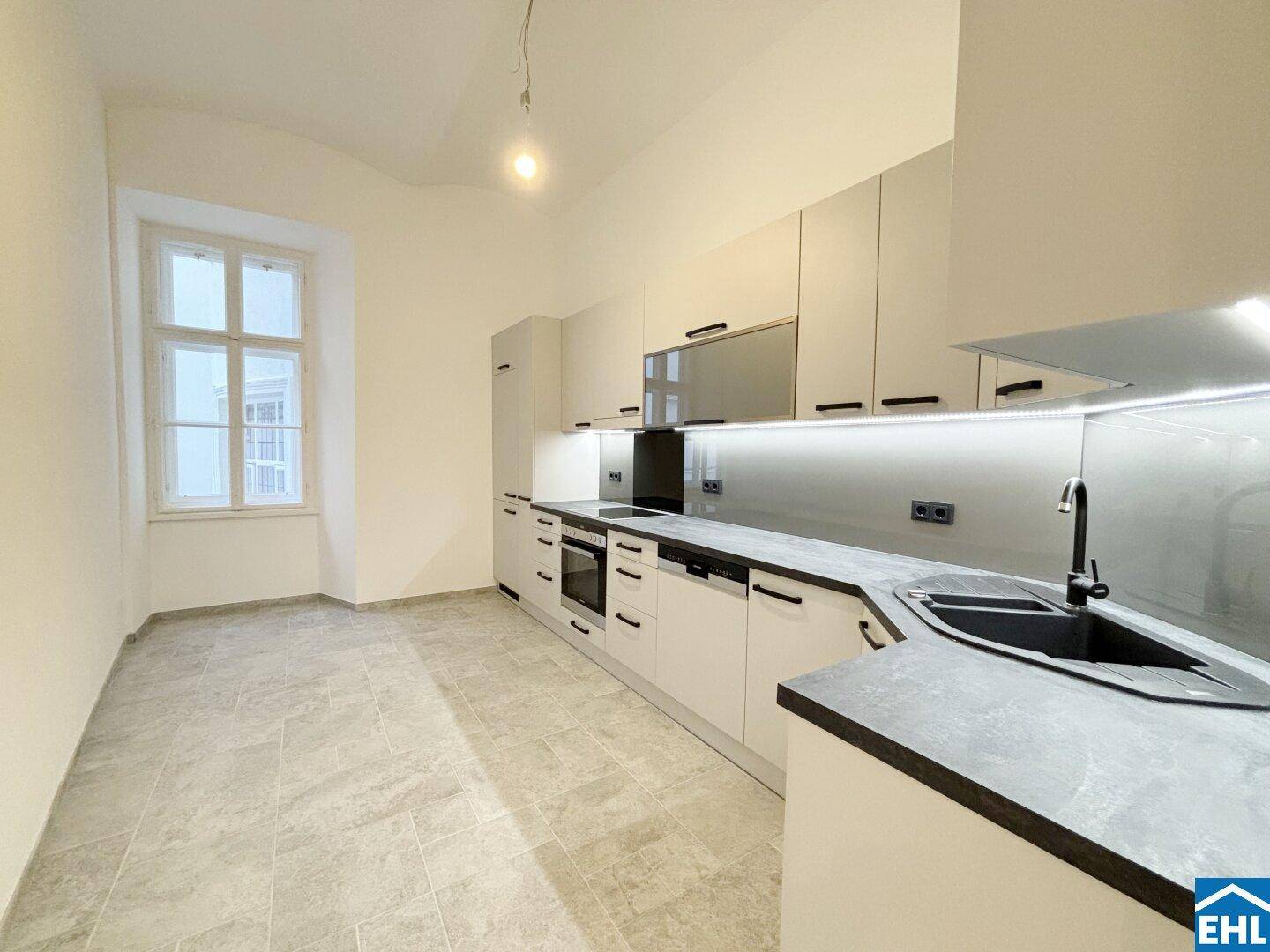 Moderne Einbauküche in Grau mit integrierten Geräten und hellem Fliesenboden.
