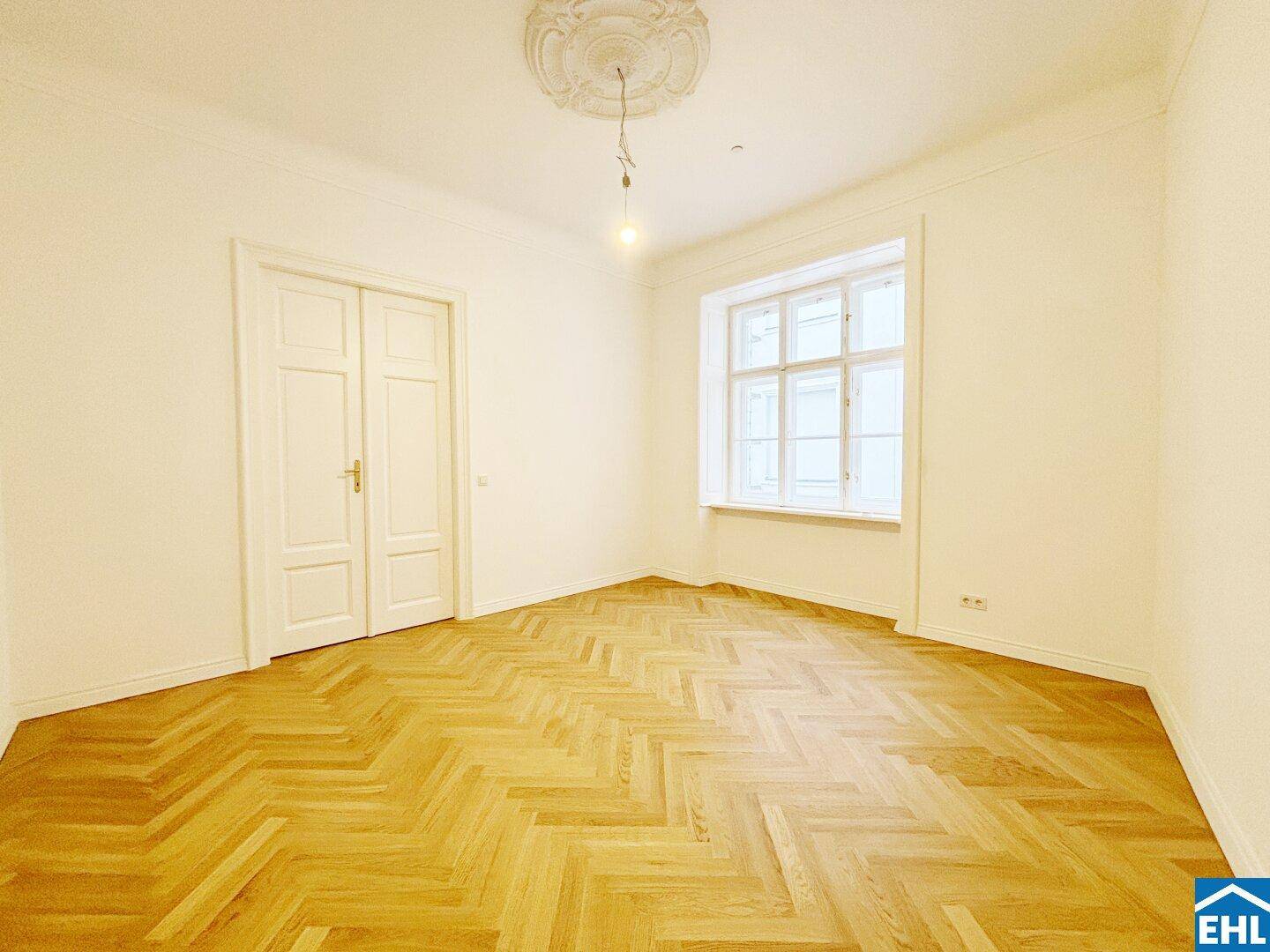 Geräumiges Zimmer mit Fischgrätparkett, hohen Decken und klassischem Fenster in einem Altbau.