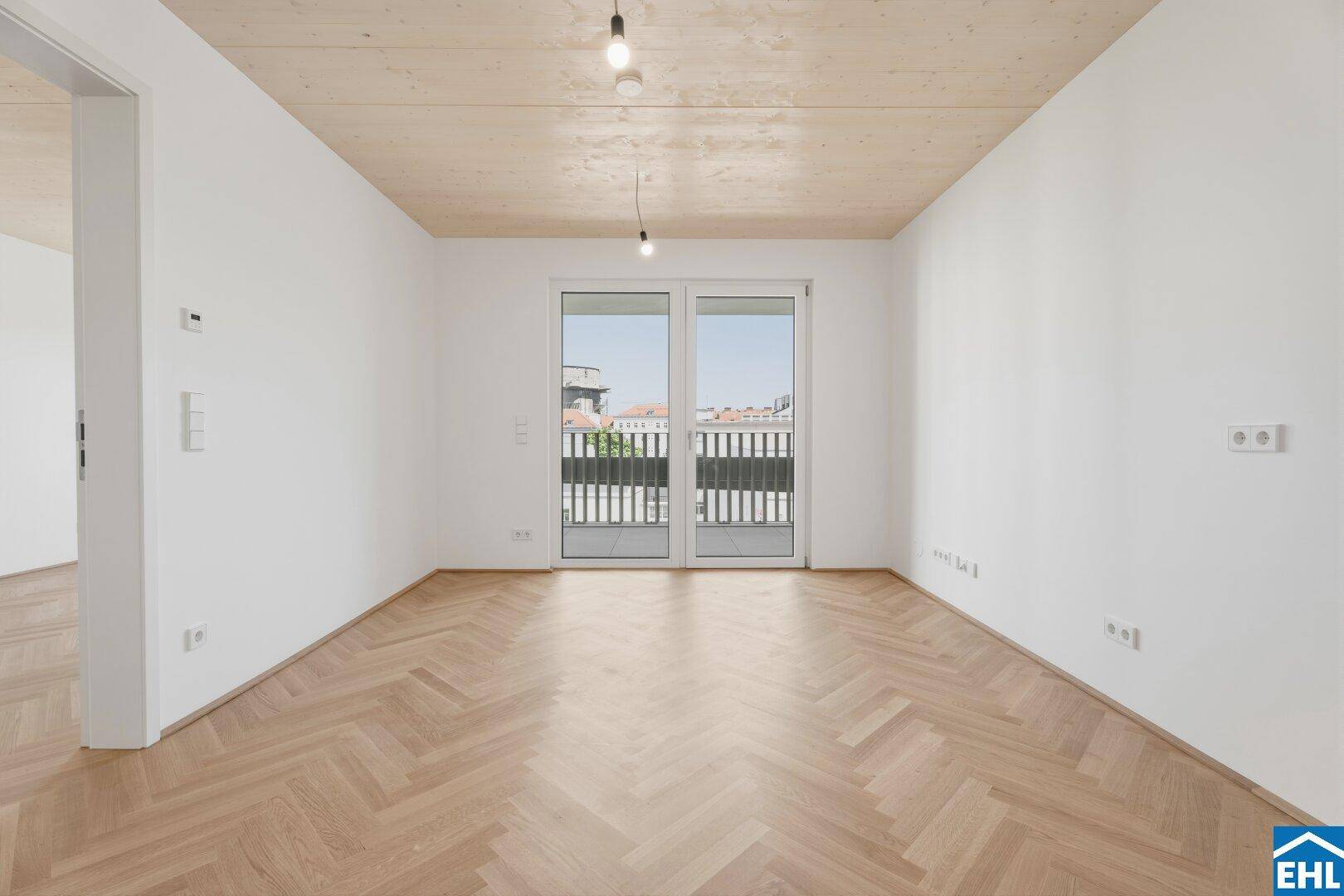 Geräumiger, heller Raum mit Fischgrätparkett und Zugang zu einem französischen Balkon.