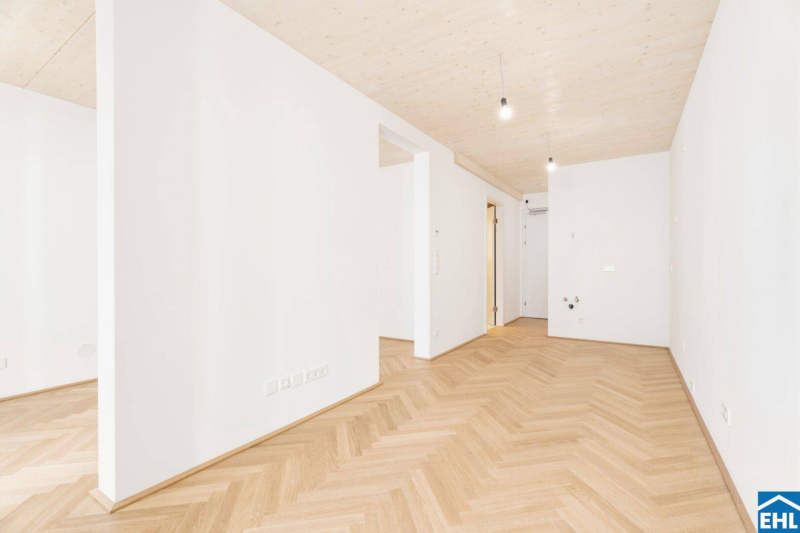 Offener Wohnbereich mit hellem Fischgrätparkett und moderner Holzbalkendecke, bereit zum Einzug.