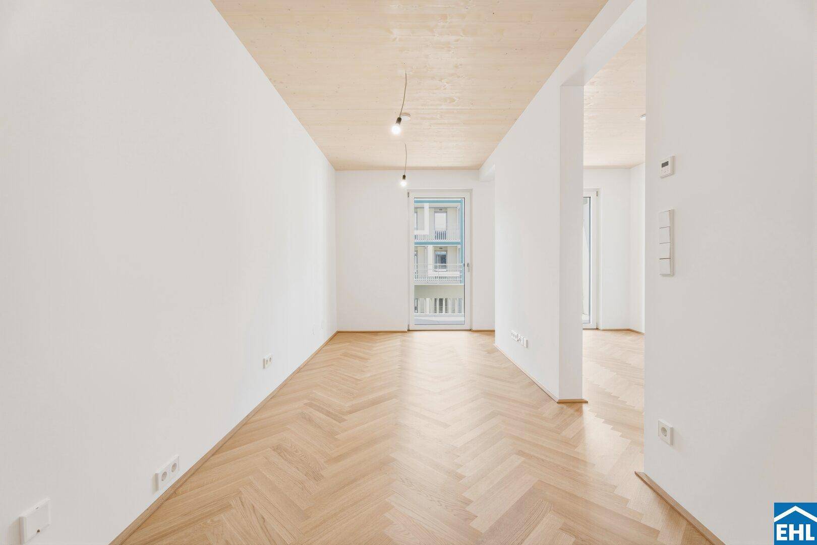 Leerer Raum mit Fischgrätparkett, Holzdecke und Zugang zu einem Balkon.