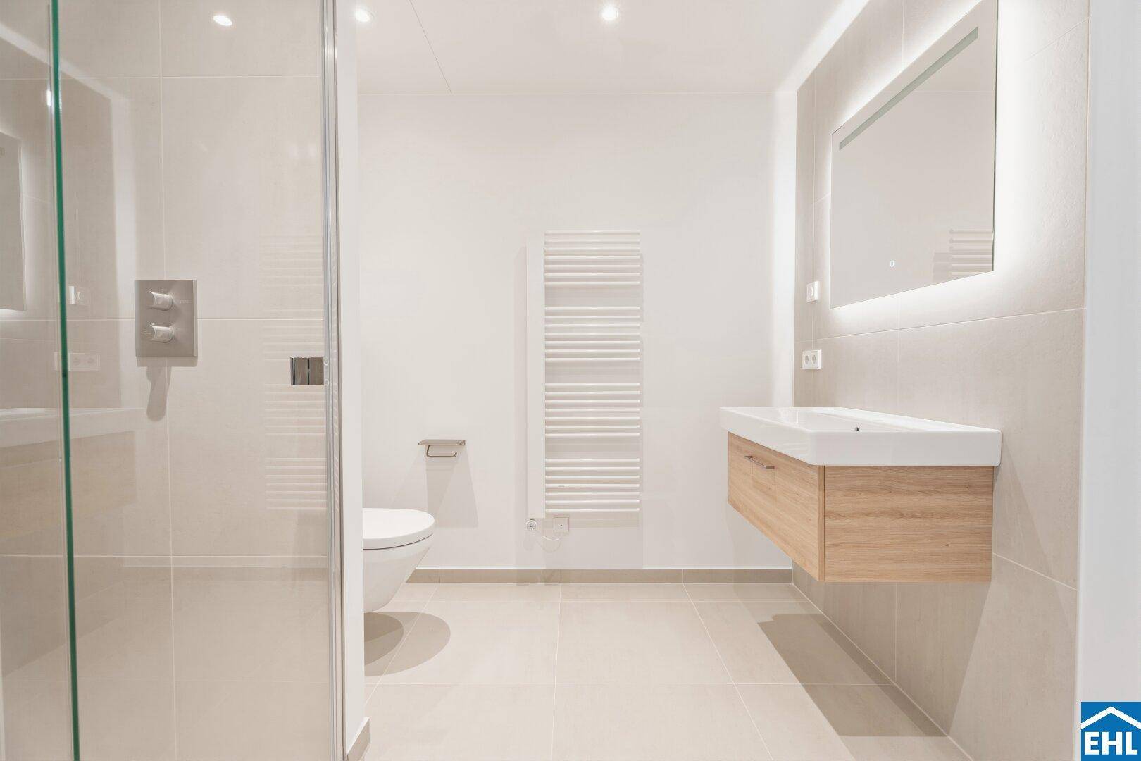 Stilvolles Badezimmer mit modernem Waschtisch, beleuchtetem Spiegel und großer Dusche.