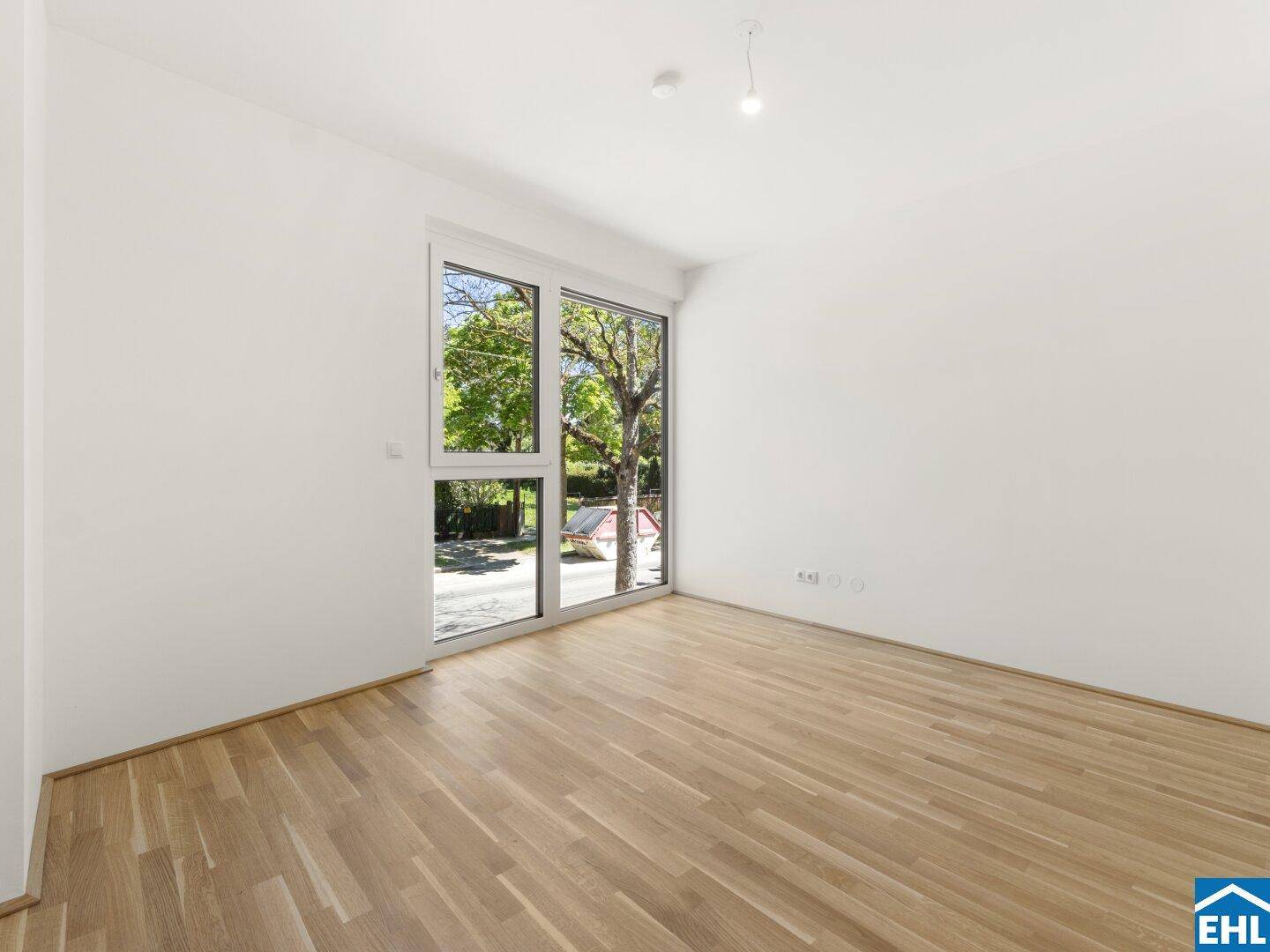 Helles Schlafzimmer mit Eichenparkett und großem Fenster mit Blick auf die Straße und Bäume.