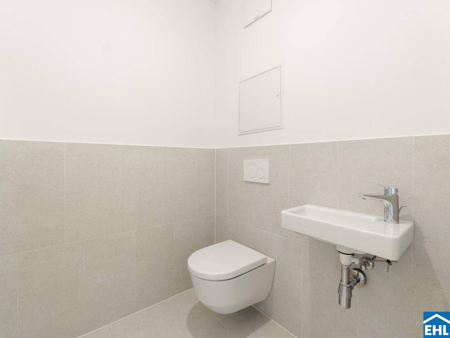 Kompaktes Gäste-WC mit wandhängender Toilette und kleinem Waschbecken in hellen Fliesen.
