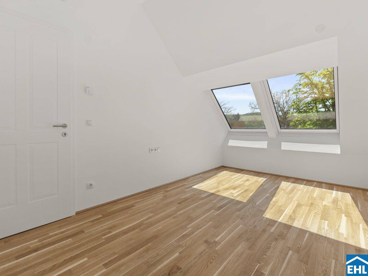 Lichtdurchflutetes Zimmer im Dachgeschoss mit Holzboden und zwei großen Dachfenstern.