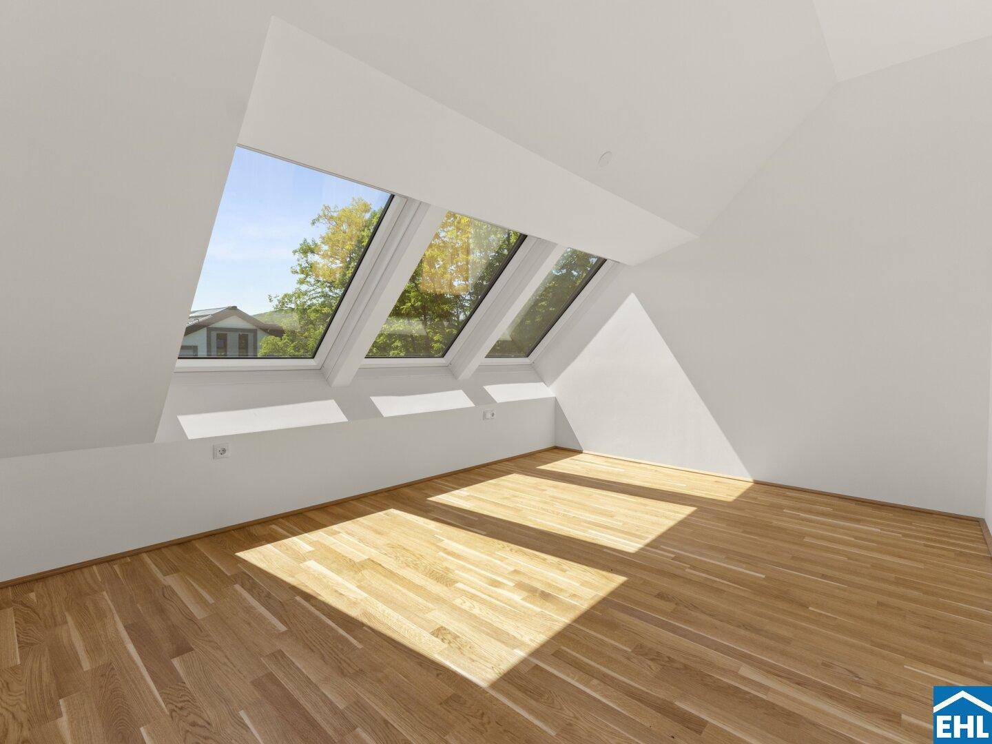 Helles Dachzimmer mit Holzboden und einer Reihe von Dachfenstern, die viel Licht hereinlassen.